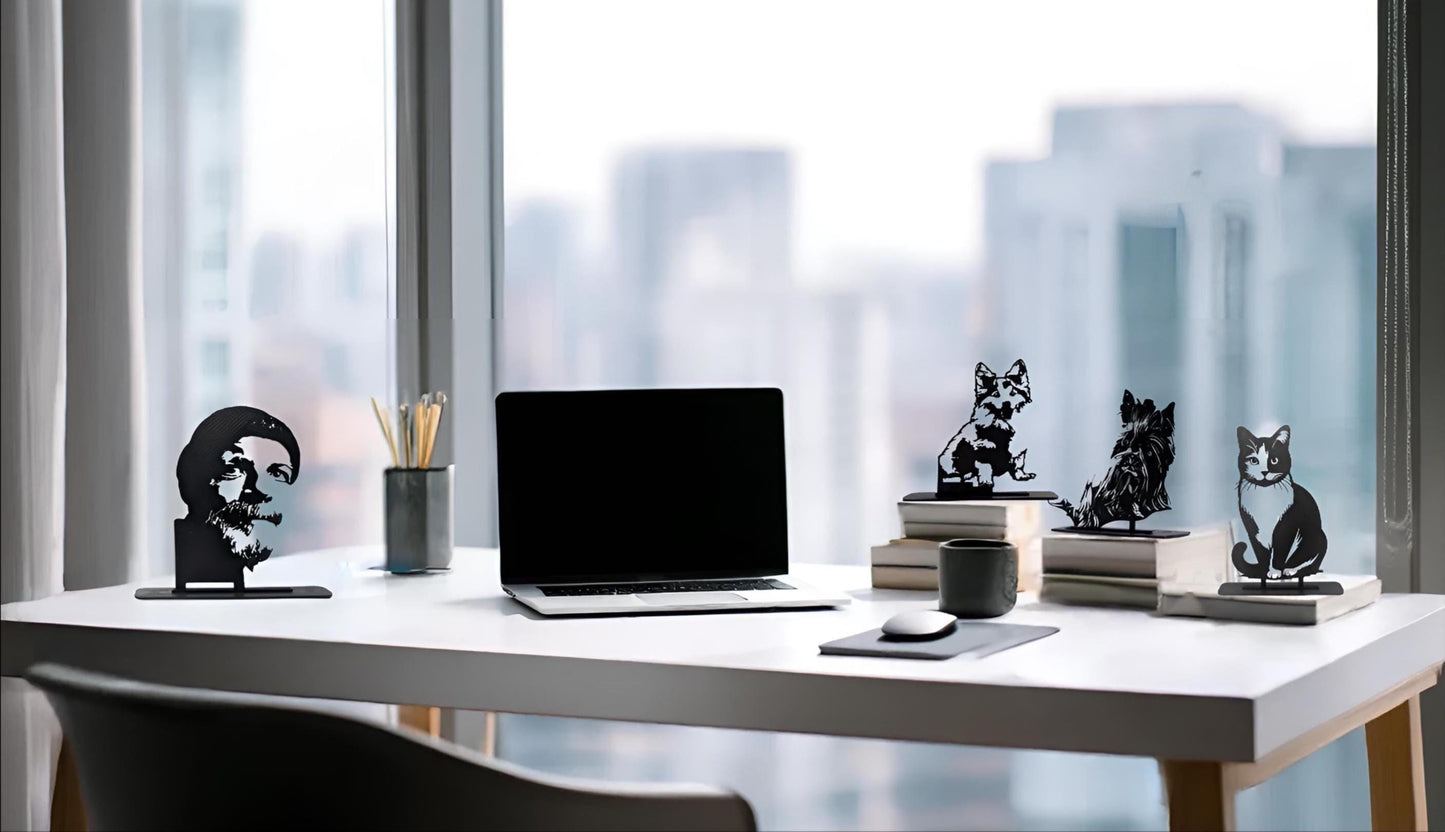 Five black 3D-printed pet silhouettes (one cat and four dogs) displayed on a modern office desk beside a laptop, mouse, coffee cup, and books, with a city skyline visible through large windows behind.